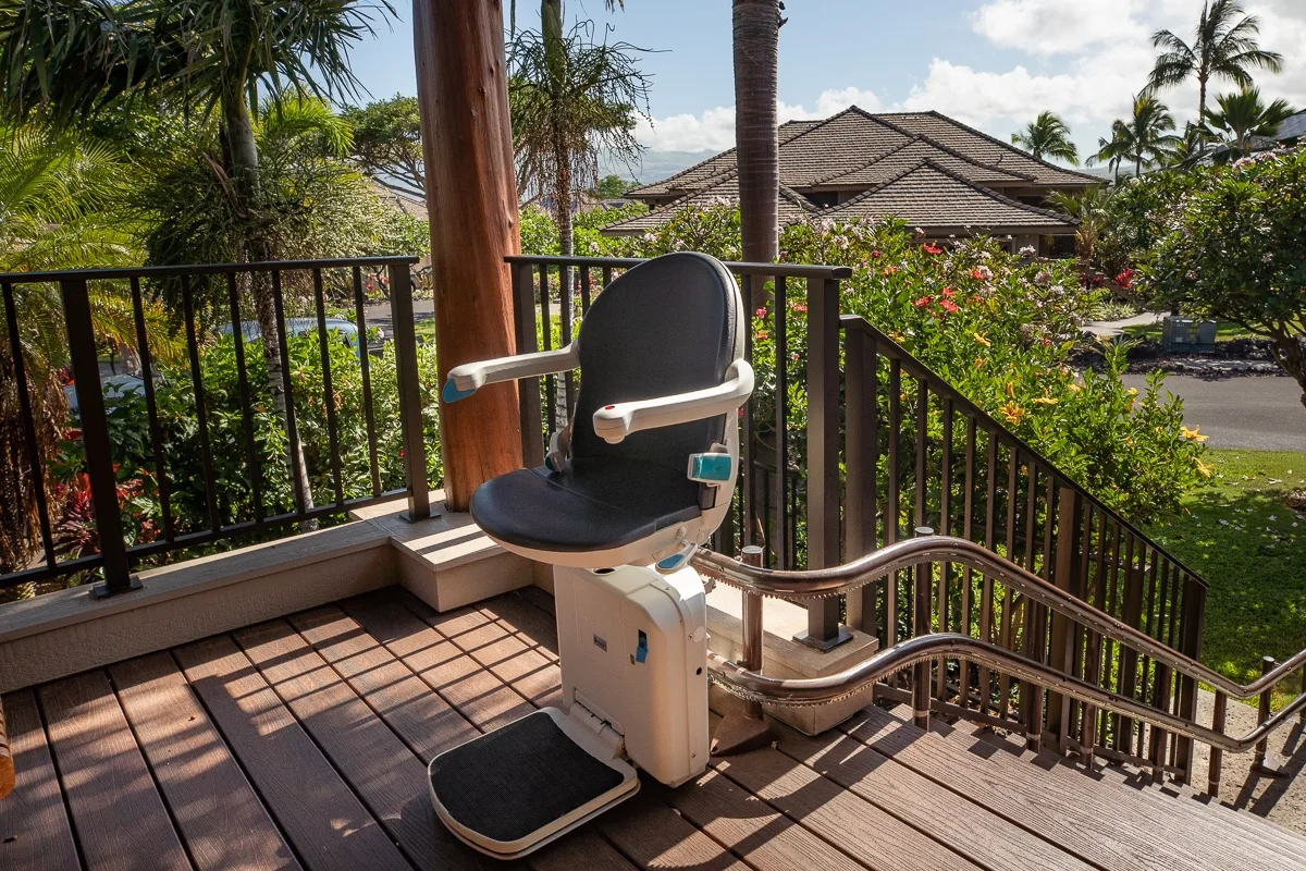 An outdoor stair lift sits on a wooden deck overlooking a garden.