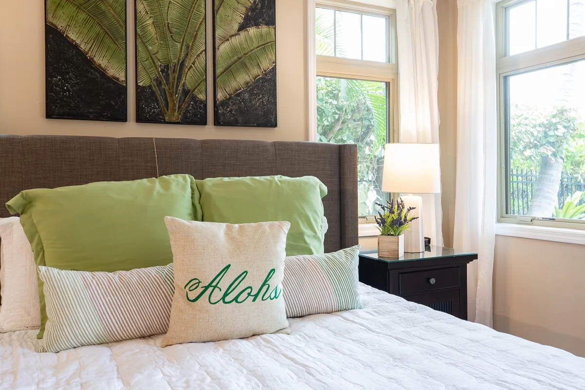 A bedroom with a bed, green pillows, and large windows.