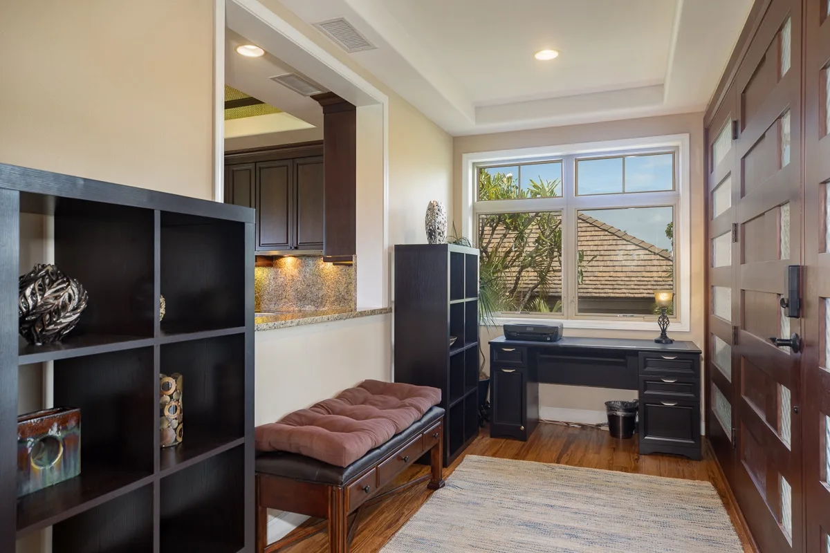 A furnished study with a desk beneath a wide window and a cushioned bench.
