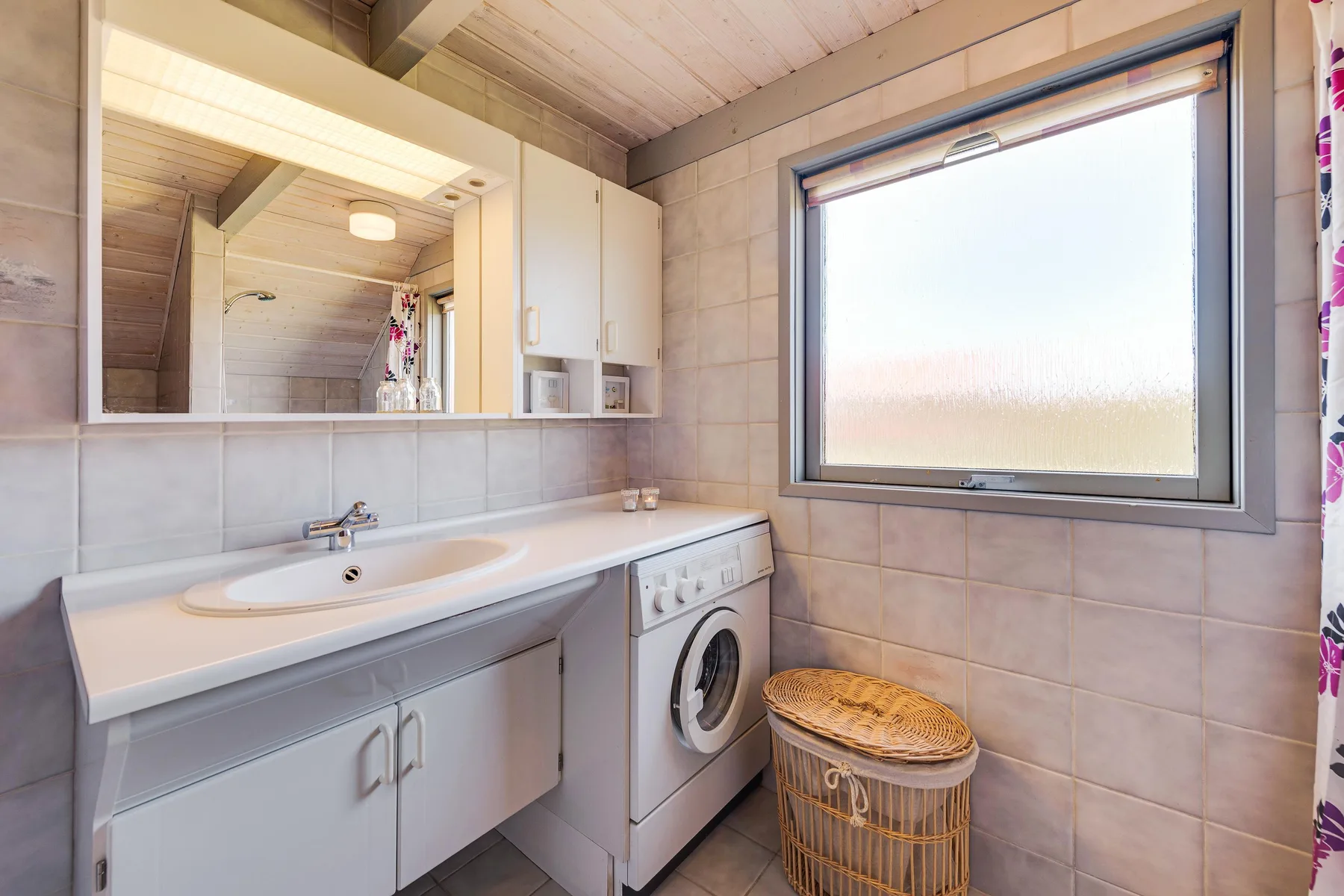 Un baño alicatado con lavabo, lavadora y una ventana grande.