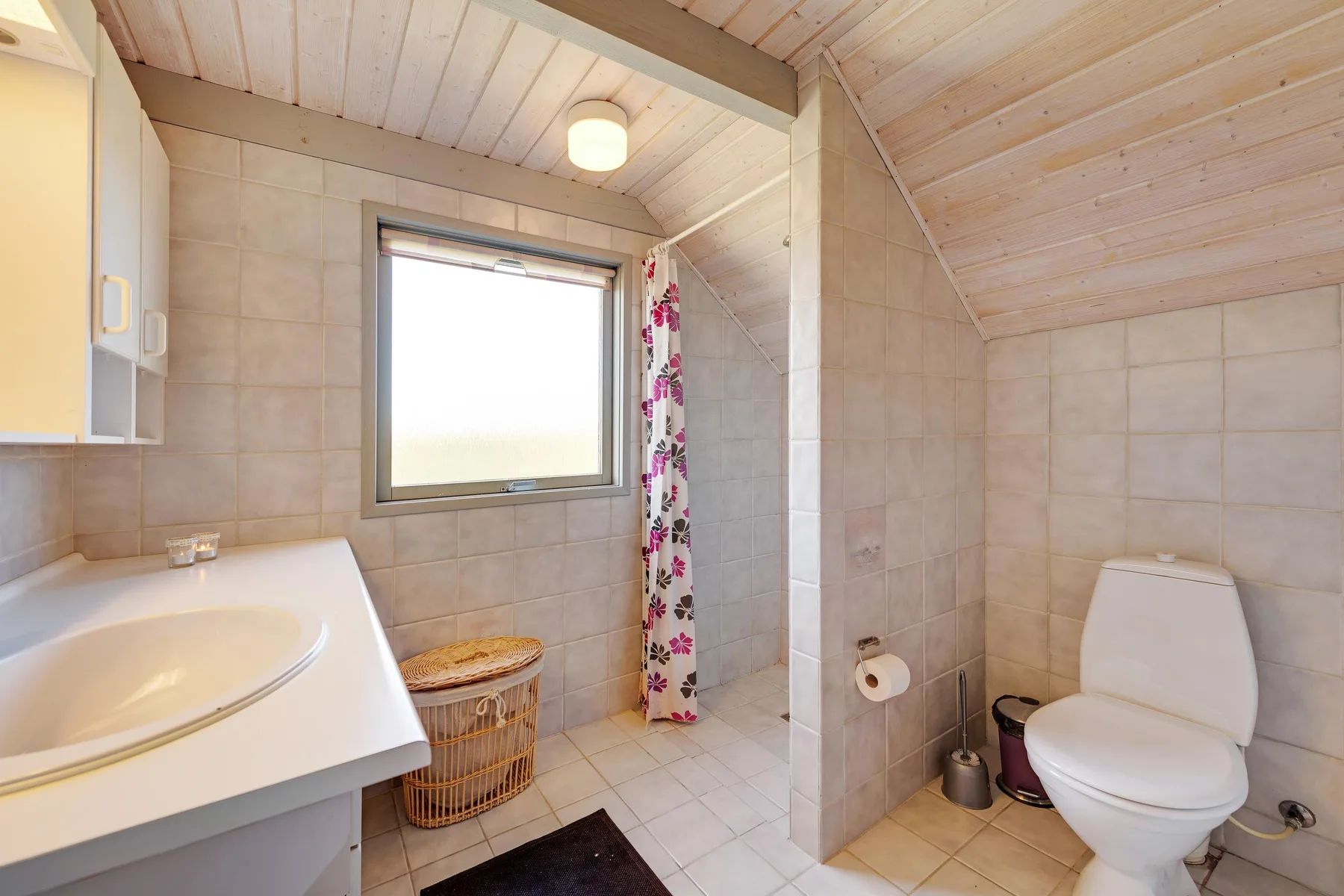 Un baño alicatado tiene un lavabo, un inodoro y una ventana.
