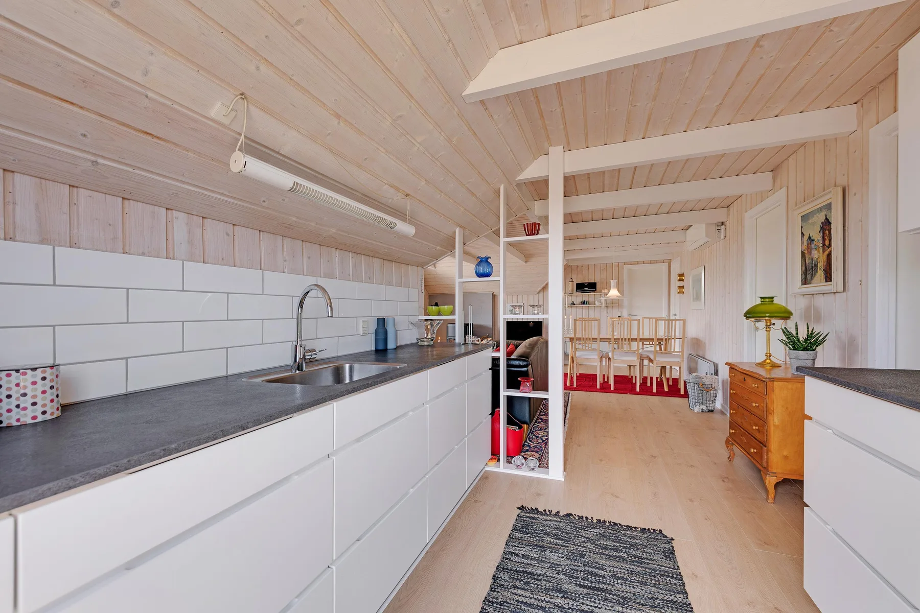 Una cocina luminosa se abre a un comedor con una encimera larga y una mesa.