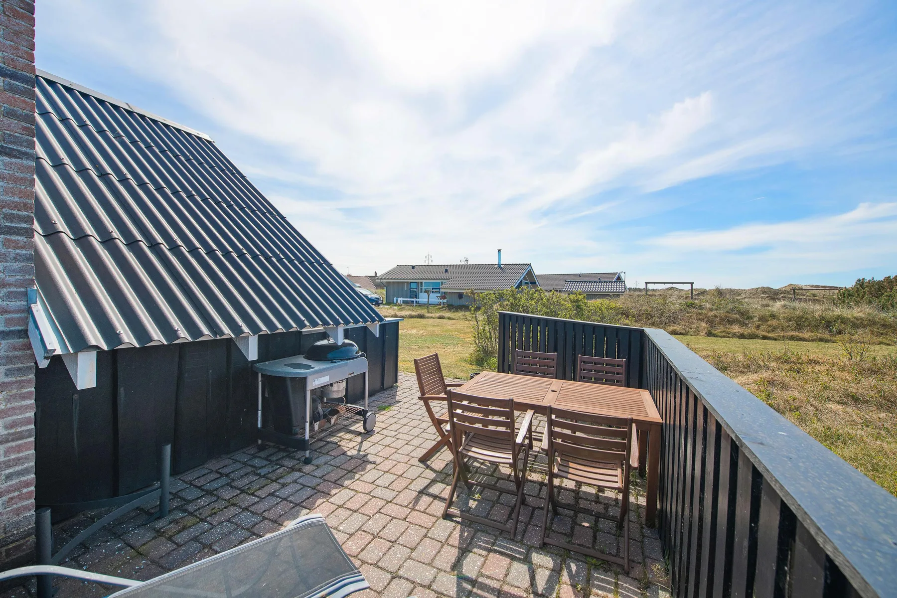 Un patio exterior pavimentado con una mesa de comedor y asientos junto a un paisaje cubierto de hierba.