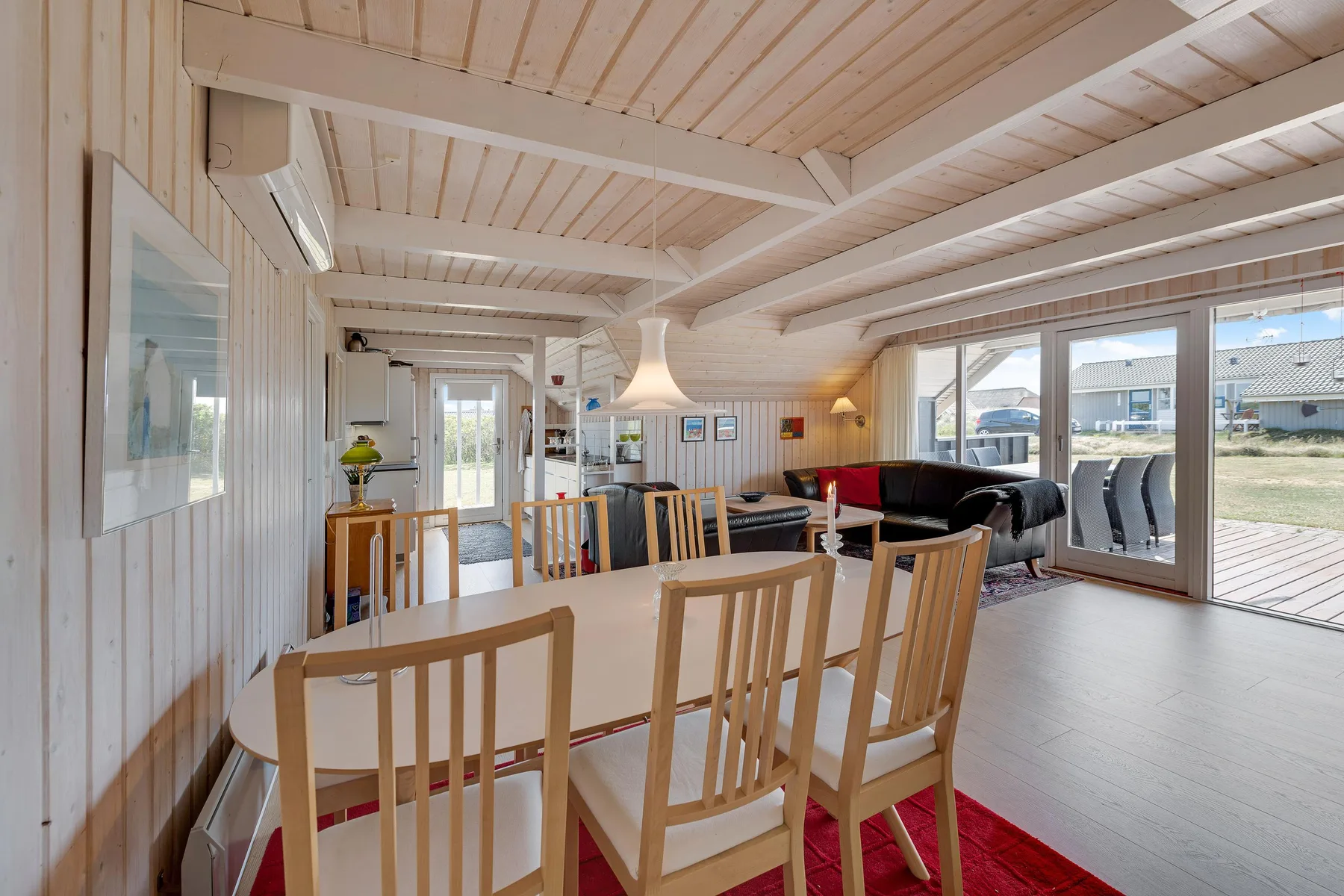 Zona luminosa de comedor y estar con una mesa, asientos y grandes ventanas.