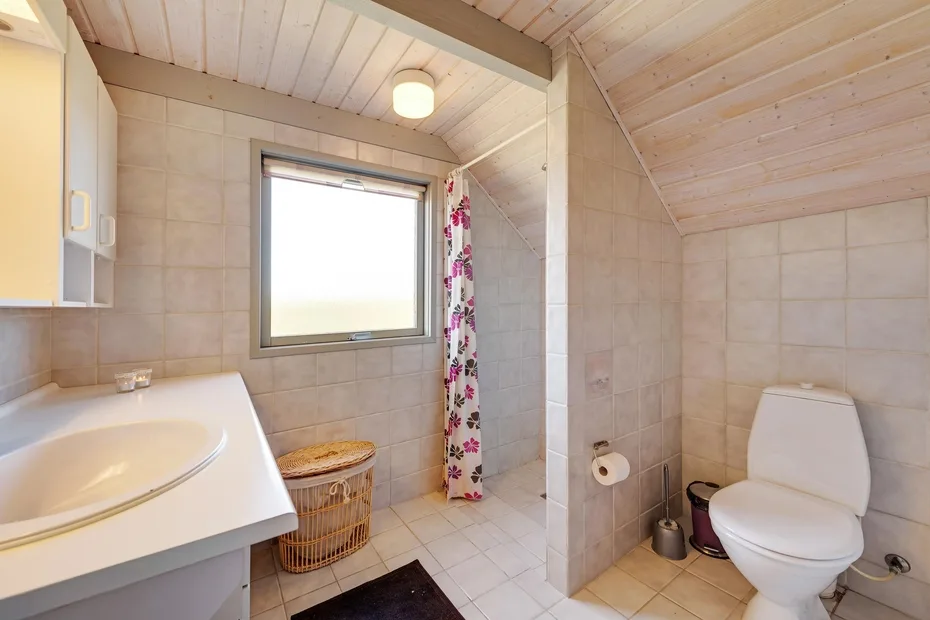 Un baño con azulejos, una ventana, cortina de ducha, lavabo e inodoro.