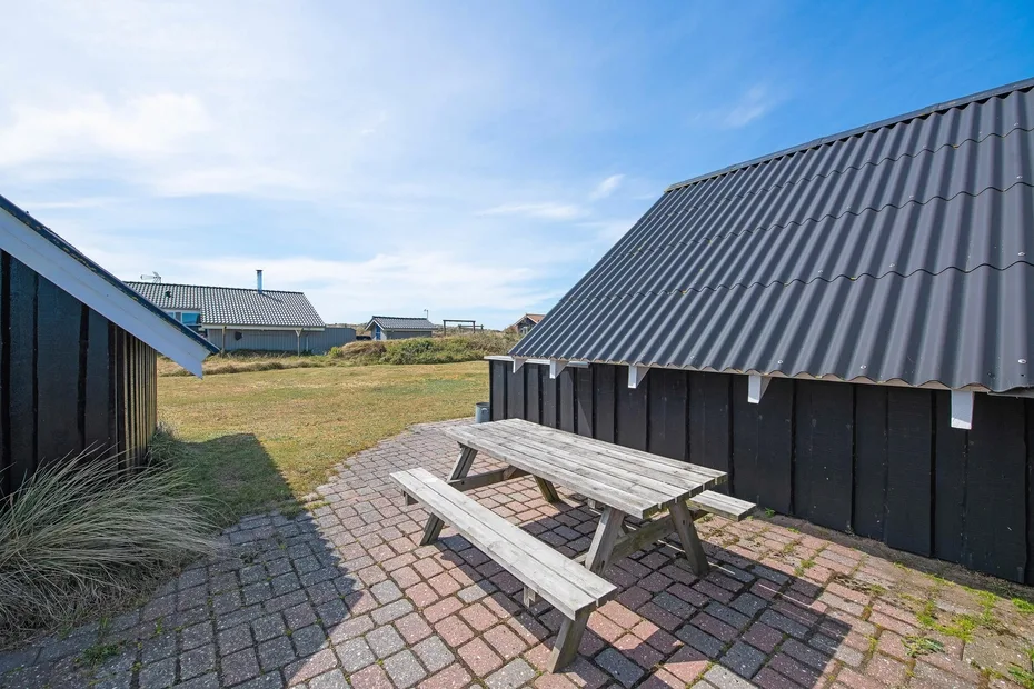 Una zona exterior pavimentada entre edificios oscuros, con una mesa de picnic de madera.