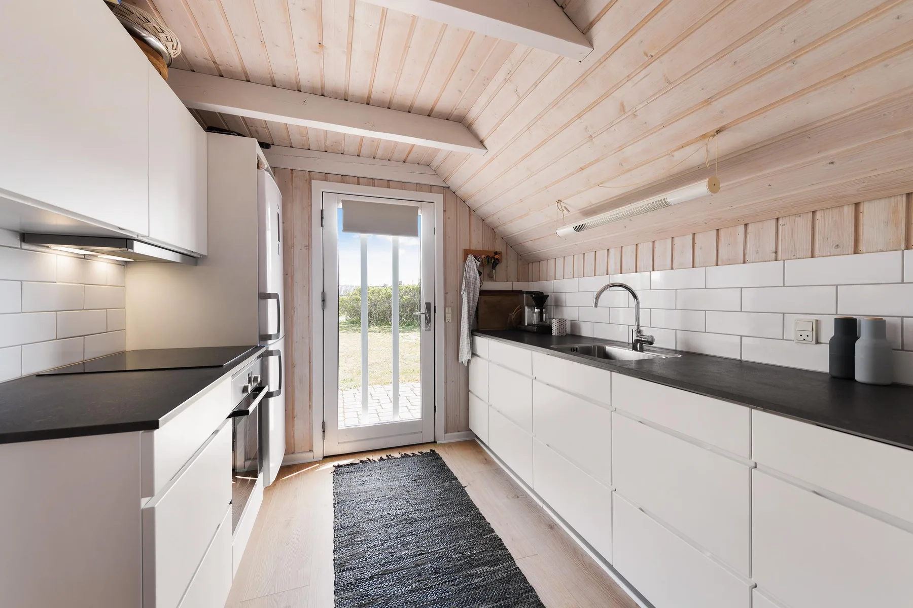 Cocina luminosa con armarios blancos, encimeras oscuras y una puerta de vidrio.