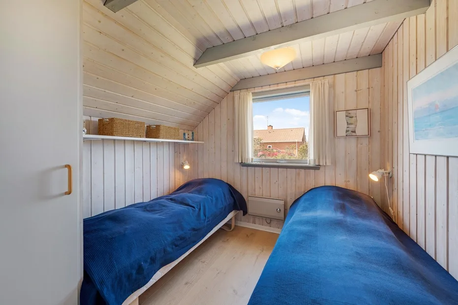Un dormitorio pequeño con dos camas cubiertas con ropa de cama azul y una ventana.