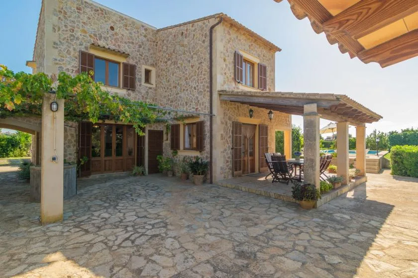 Exterior de una casa de piedra con patio pavimentado y zona de estar cubierta.