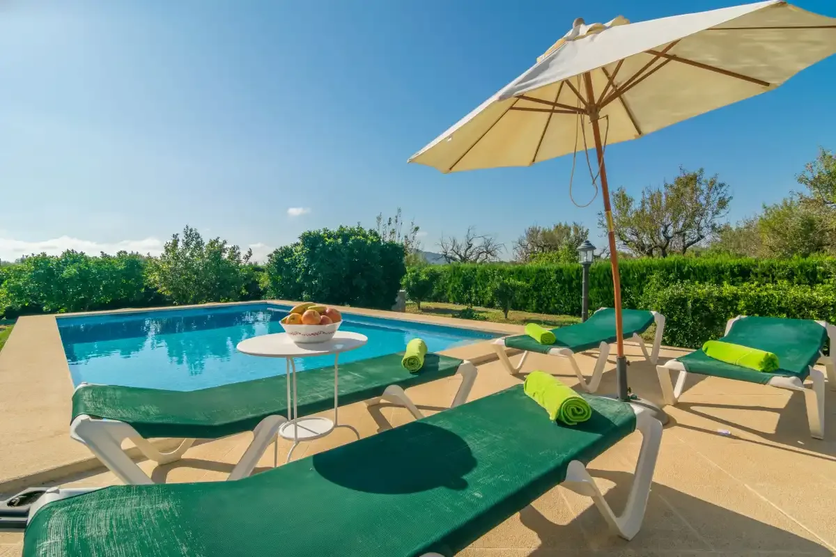 Una terraza soleada junto a la piscina, con tumbonas verdes y una sombrilla grande.