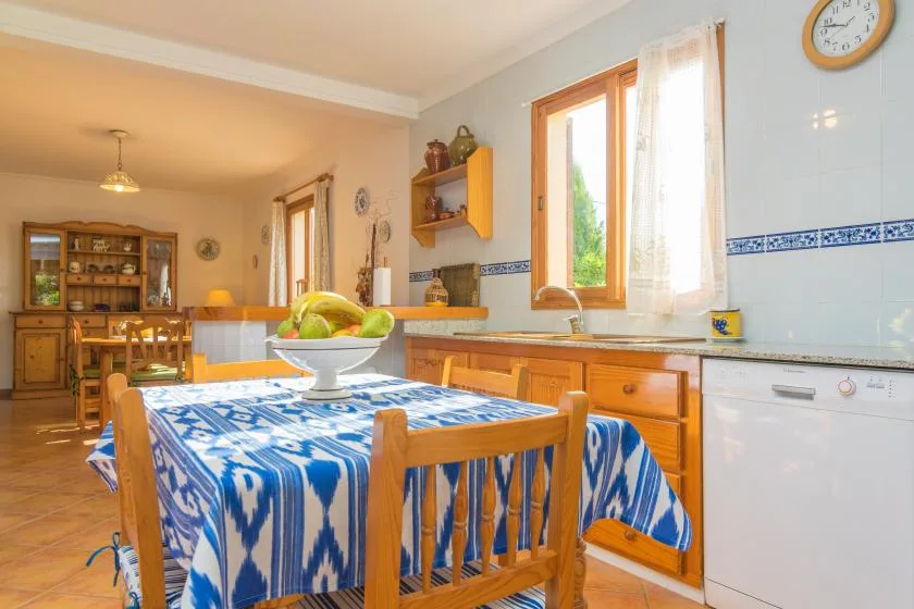 Una luminosa cocina con zona de comedor, mantel estampado azul y muebles de madera.