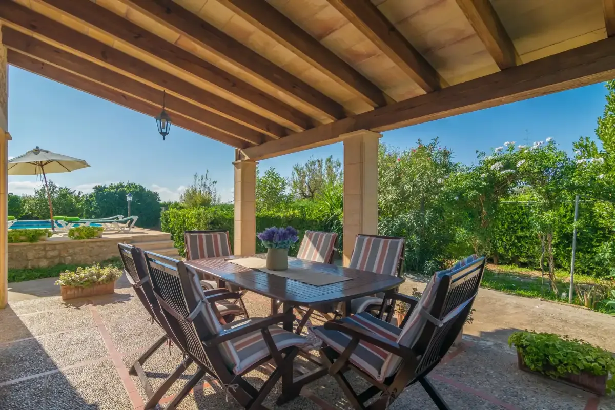 Comedor exterior cubierto con una mesa y asientos acolchados junto al jardín.