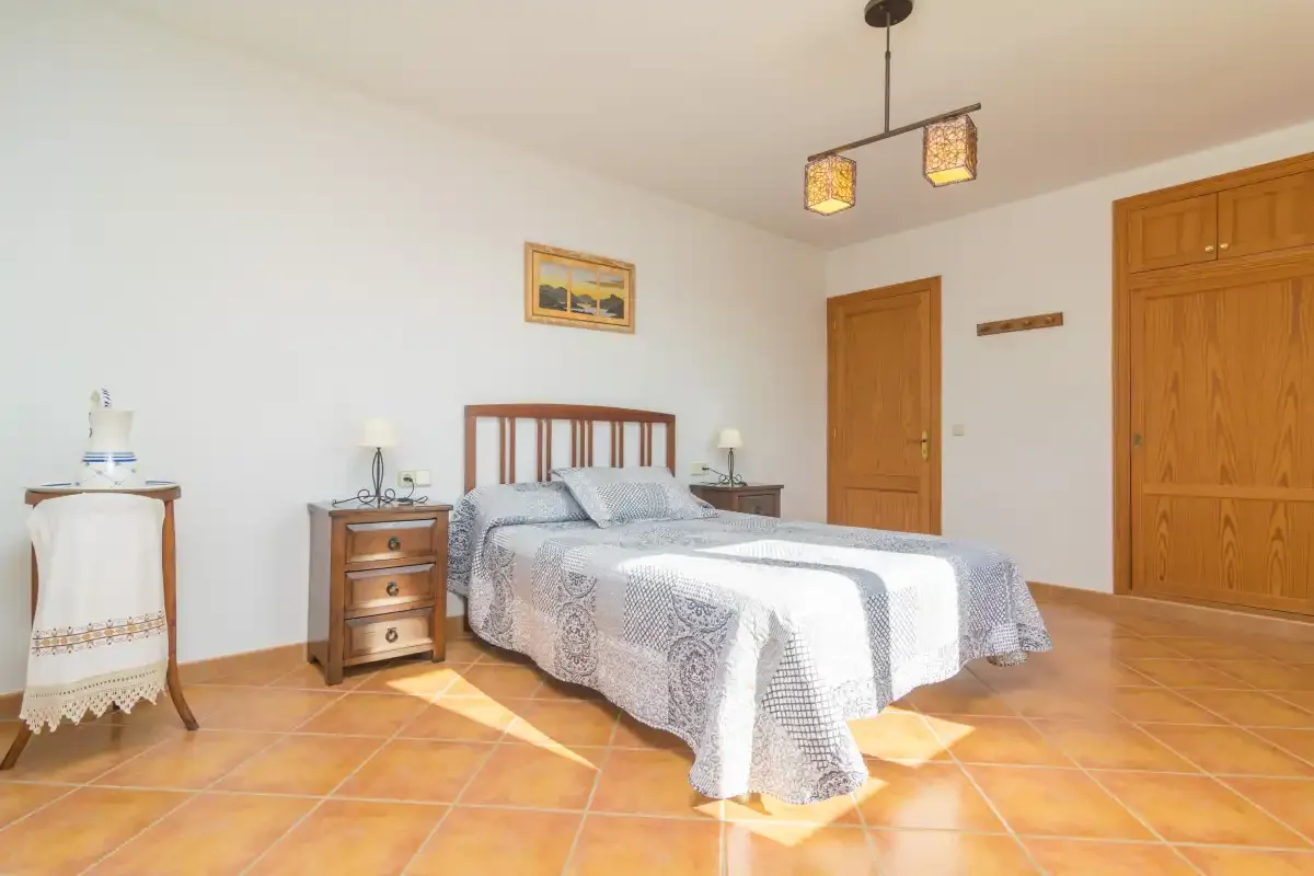 Un dormitorio con cama doble, mesitas de madera y suelo de baldosas de terracota.