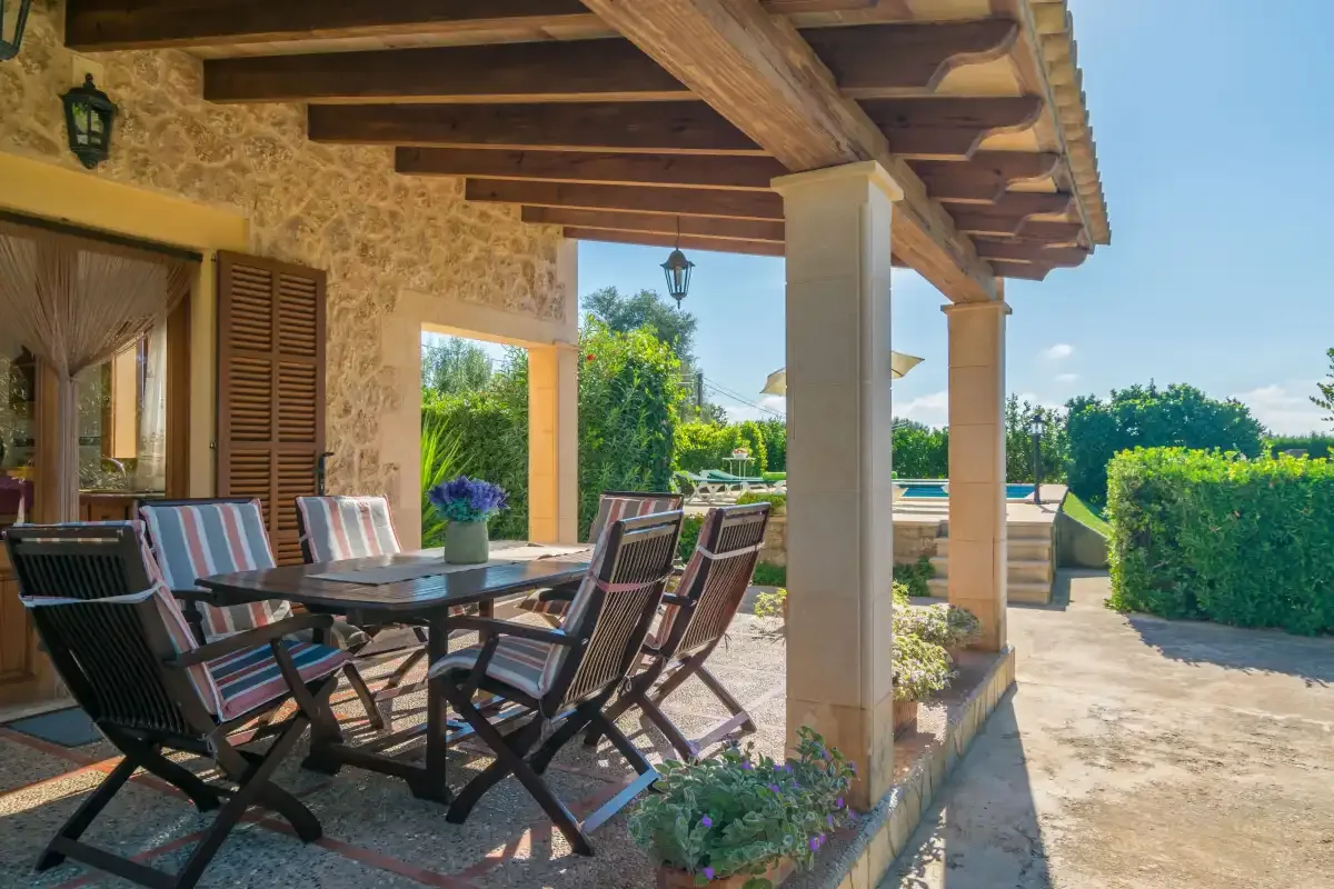 Una zona de comedor exterior cubierta, con mesa y sillas junto a un jardín.