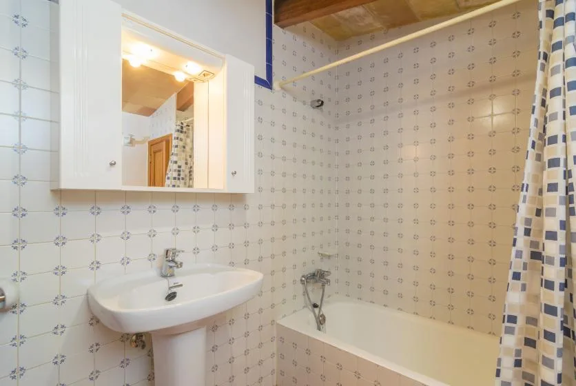 Un baño alicatado con lavabo, bañera y cortina de ducha estampada.