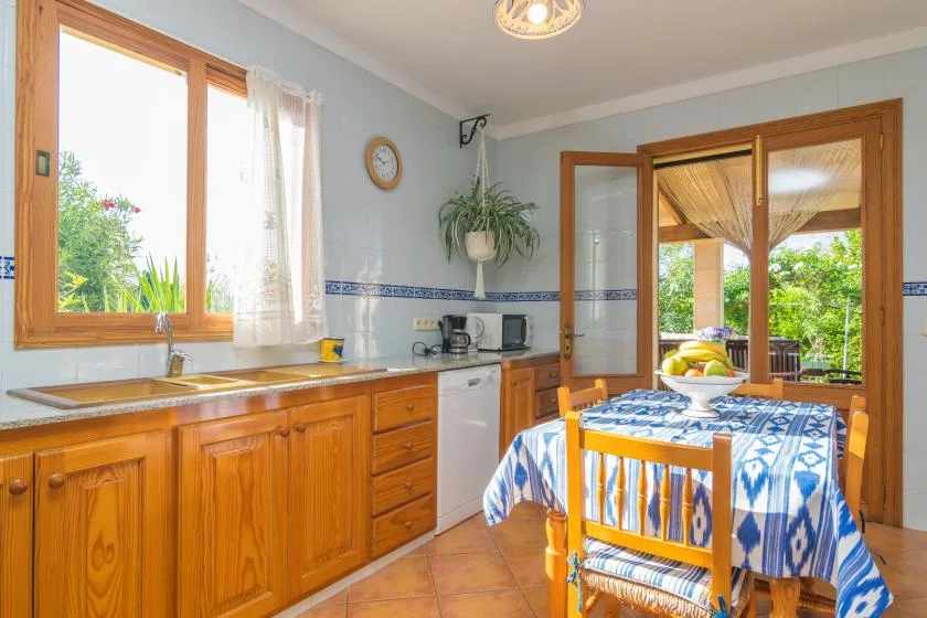 Una cocina luminosa con armarios de madera, una mesa de comedor y ventanas grandes.