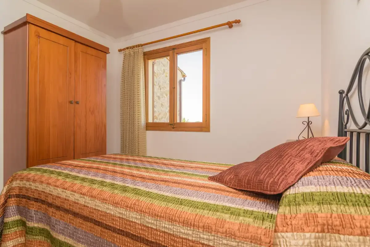 Un dormitorio con un armario de madera y una cama cubierta con una colcha a rayas.