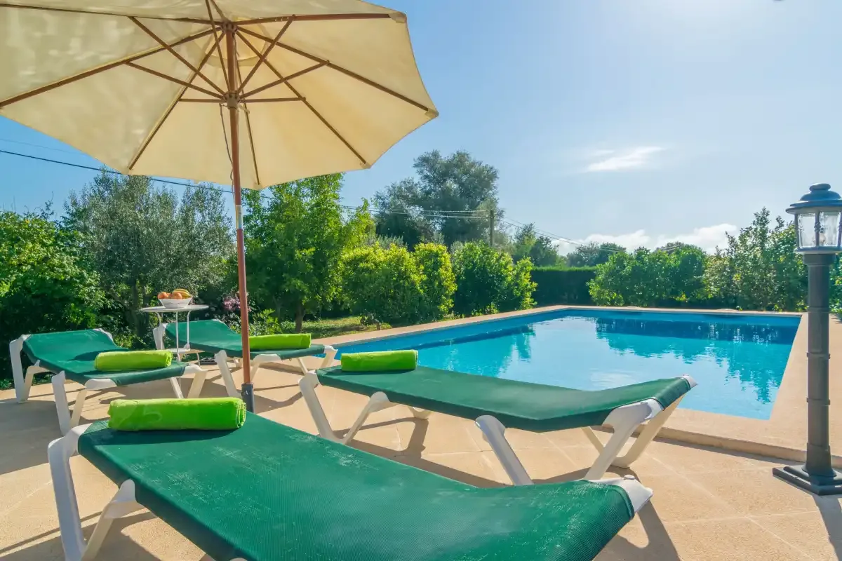 Una piscina al aire libre con tumbonas verdes y una gran sombrilla.