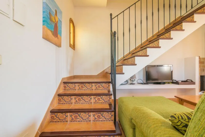 Una sala de estar con un sofá verde bajo una escalera y un televisor.