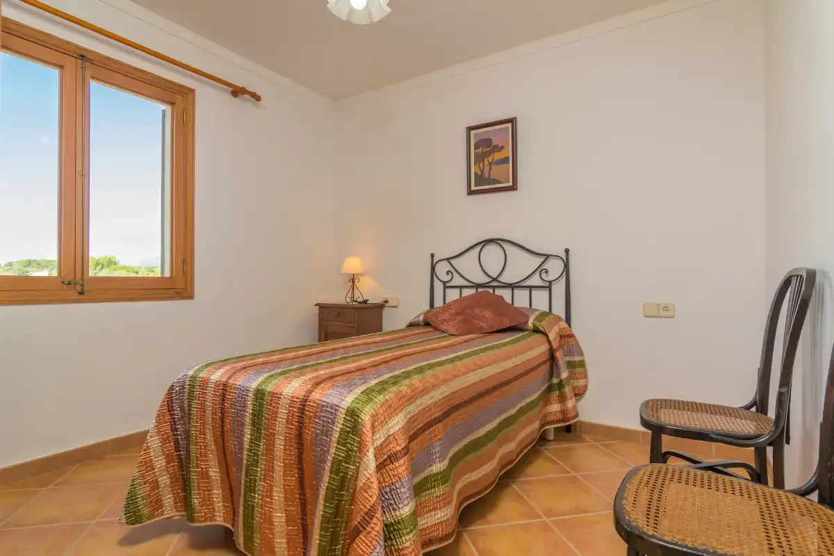 Dormitorio con una cama individual, una mesita de noche y una ventana.