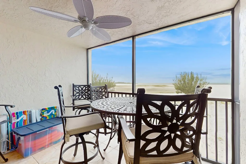 A covered patio dining area with a table and chairs overlooks the beach.