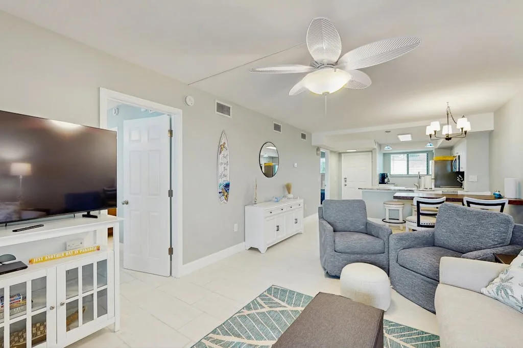 A bright living room opens into a kitchen, with seating and a television.