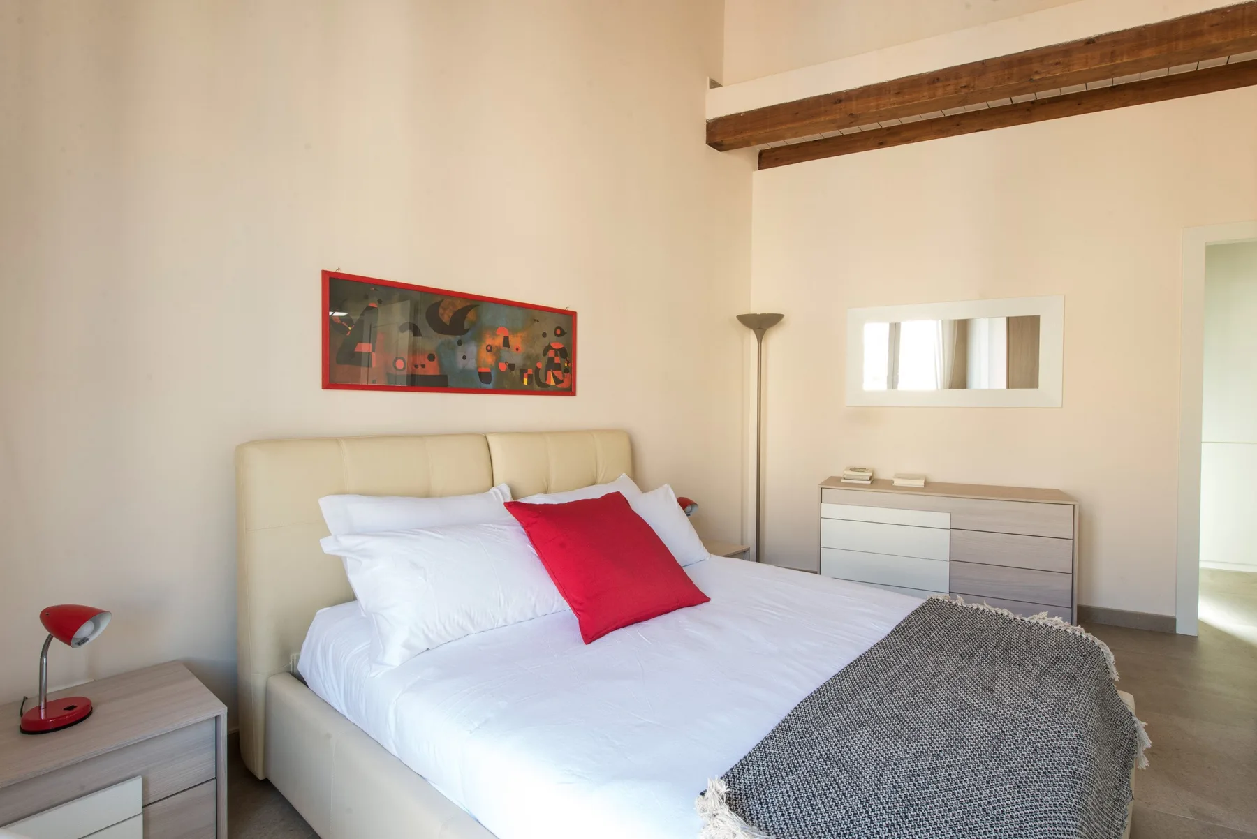 Un dormitorio con una cama, ropa de cama blanca y un cojín rojo.