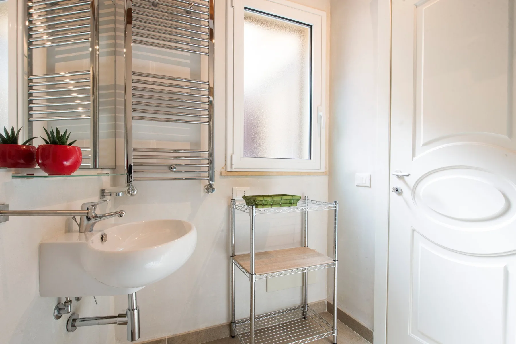 Un baño luminoso con un lavabo de pared, un toallero metálico y una pequeña estantería.