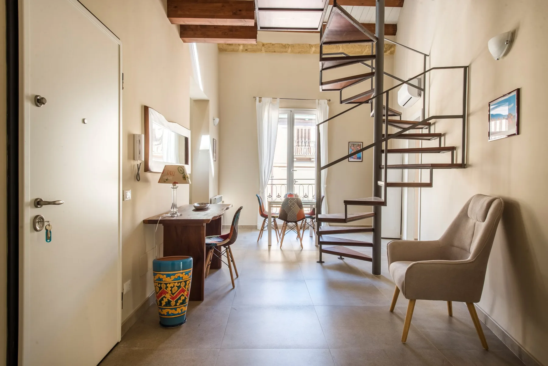 Una habitación luminosa con una escalera de caracol, un escritorio y asientos junto a la ventana.