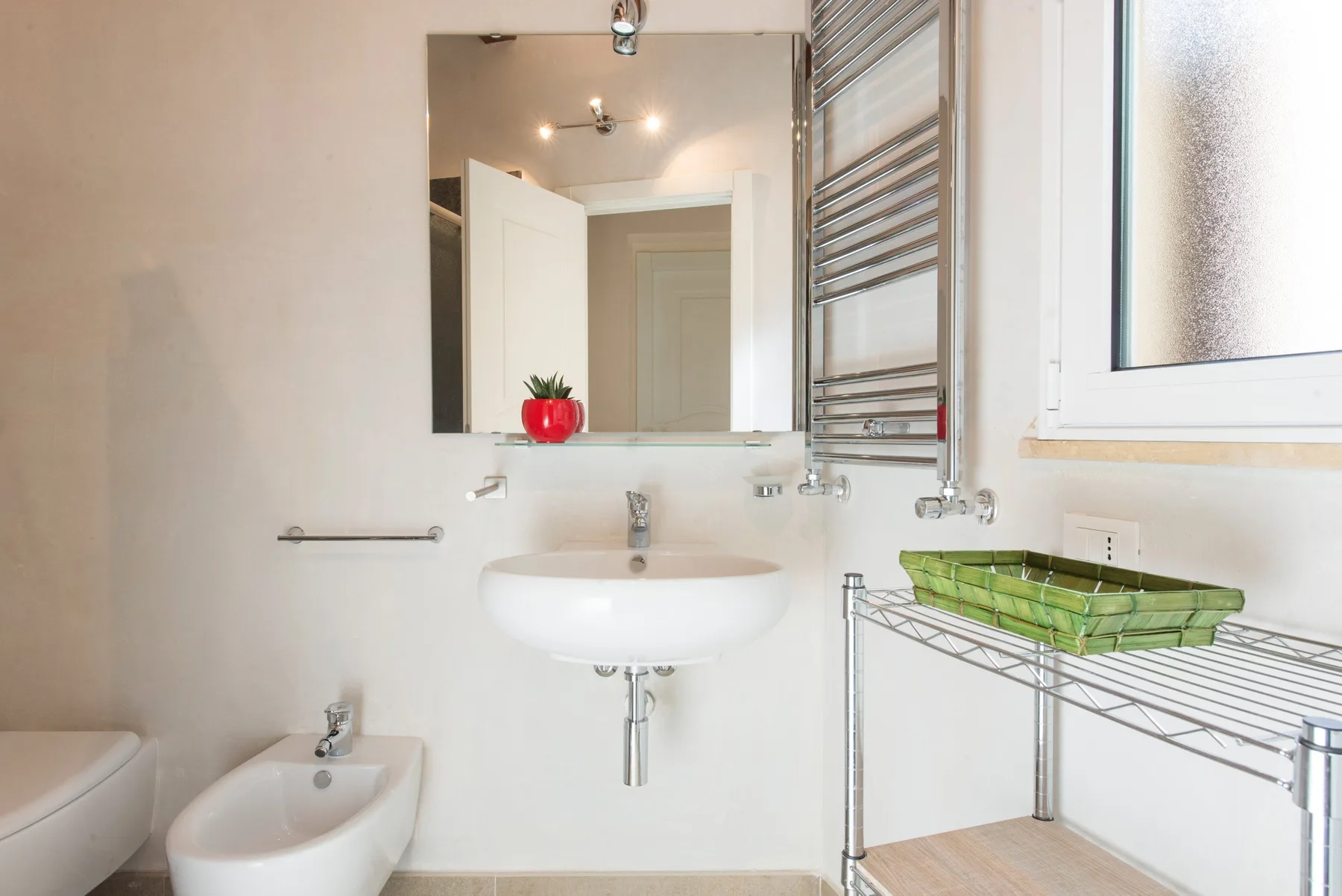 Un baño luminoso con lavabo de pared, espejo y toallero metálico.