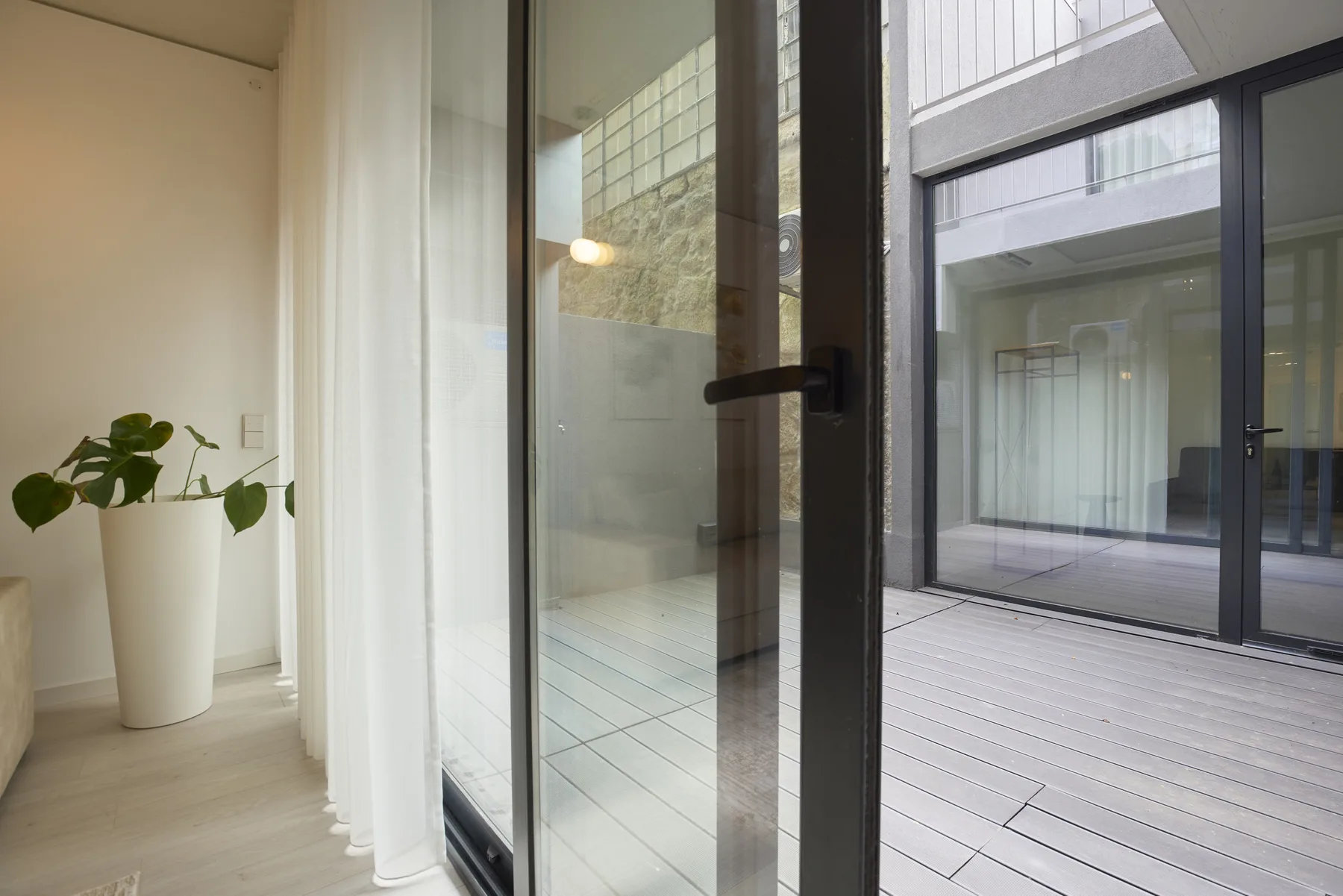 A glass door opens onto a tiled courtyard beside a bright interior with a potted plant.