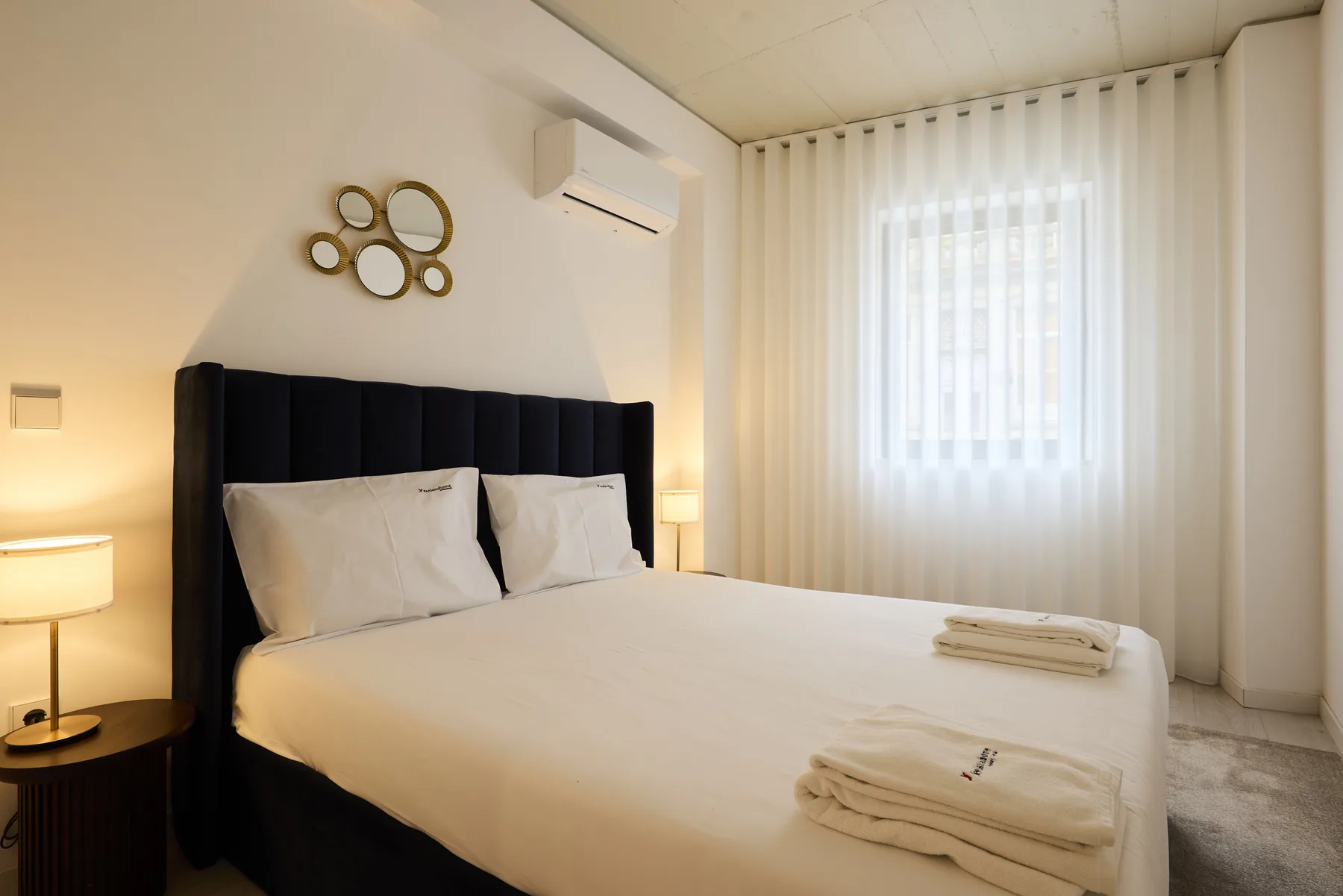 A bedroom with a large bed and a window covered by sheer curtains.