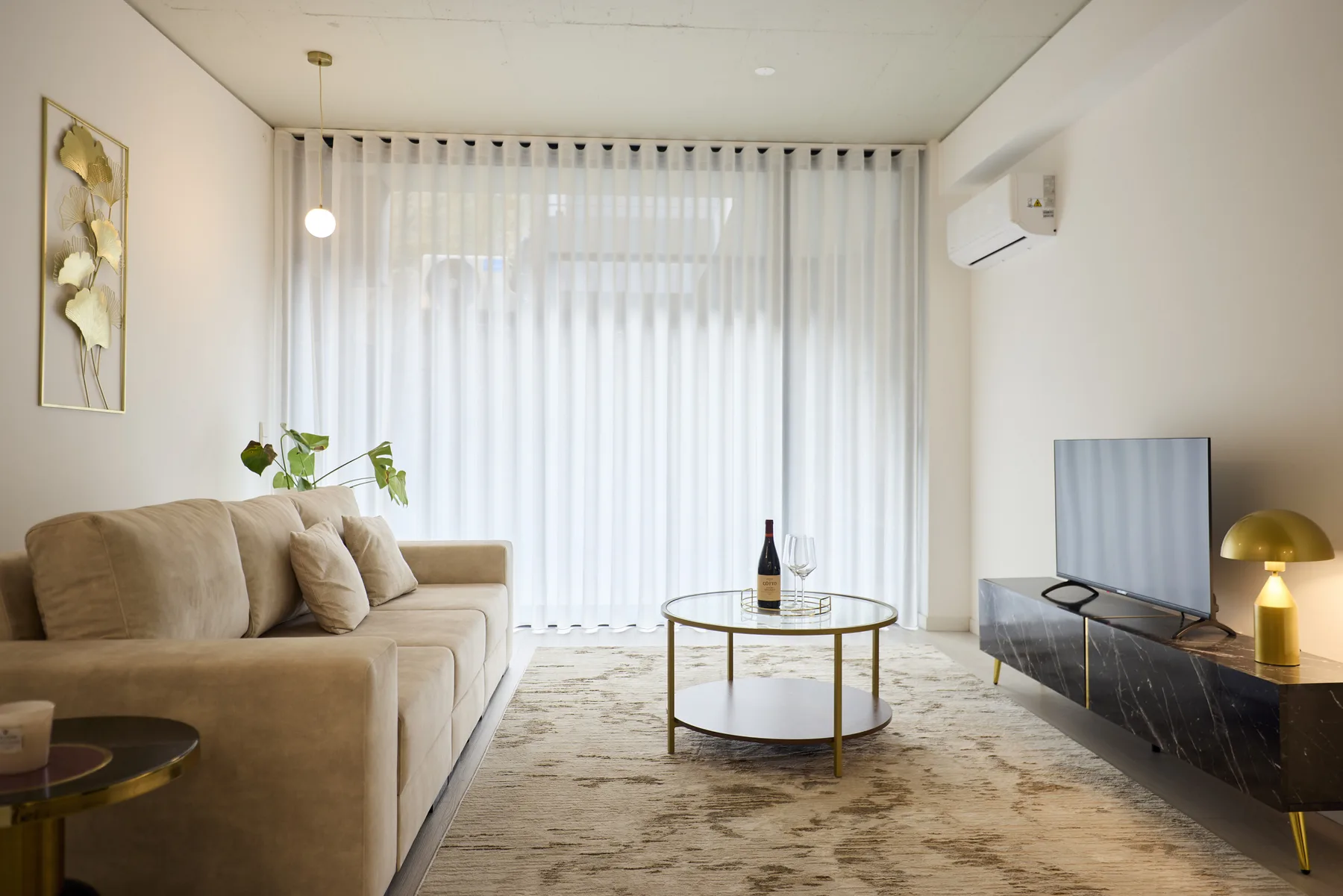 A living room with a beige sofa, a round coffee table, and sheer curtains.
