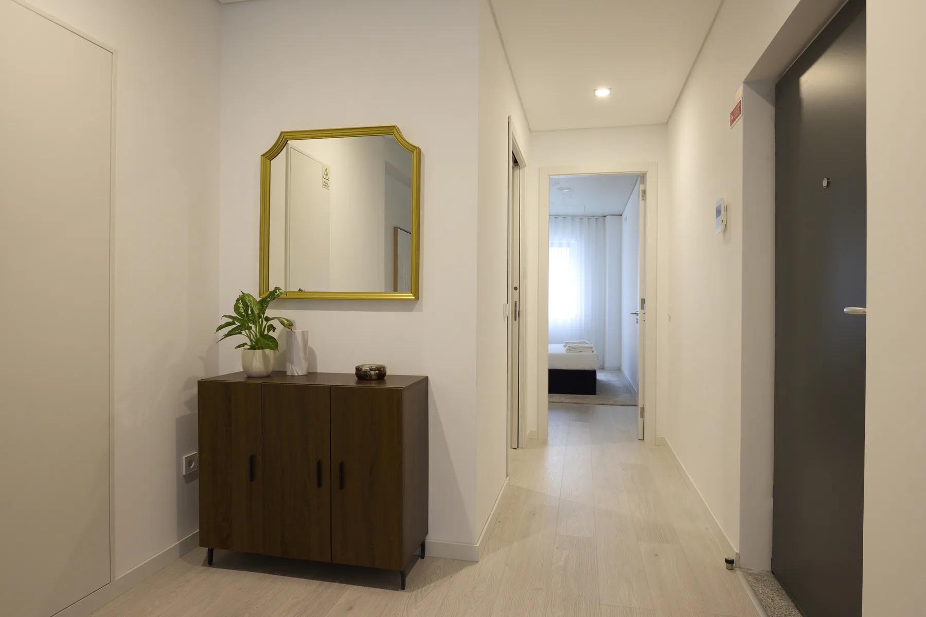 A bright hallway with a wooden cabinet and mirror beside an open doorway.