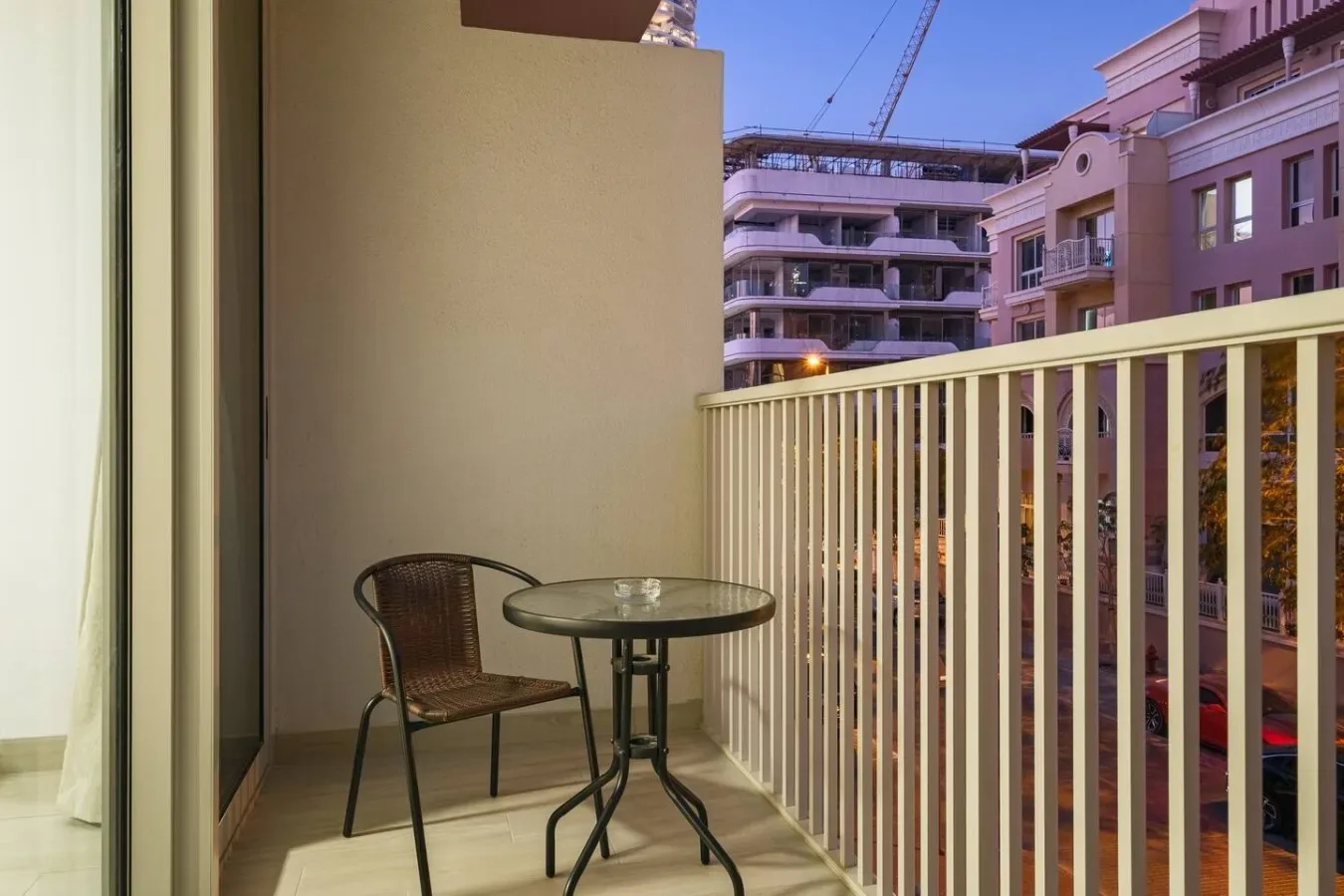 A small balcony with a round table and seating overlooks nearby buildings.