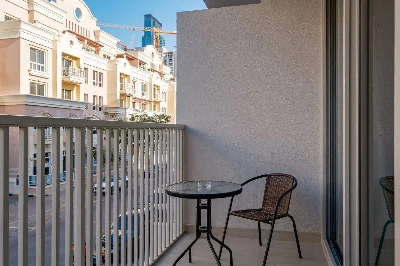 A small balcony has a table and seating beside a sliding glass door.