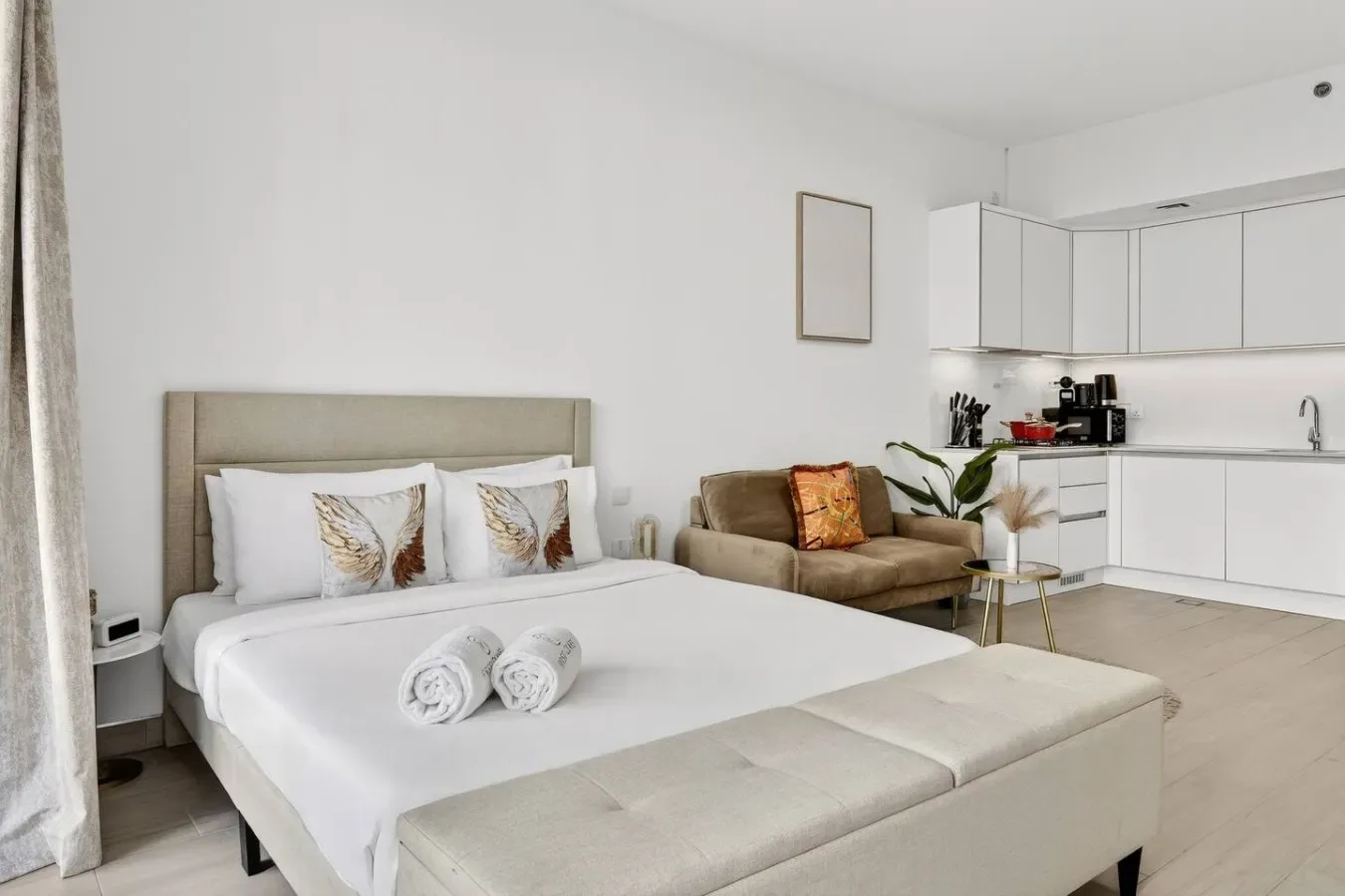 A bedroom with a double bed, a small seating area, and a kitchenette.