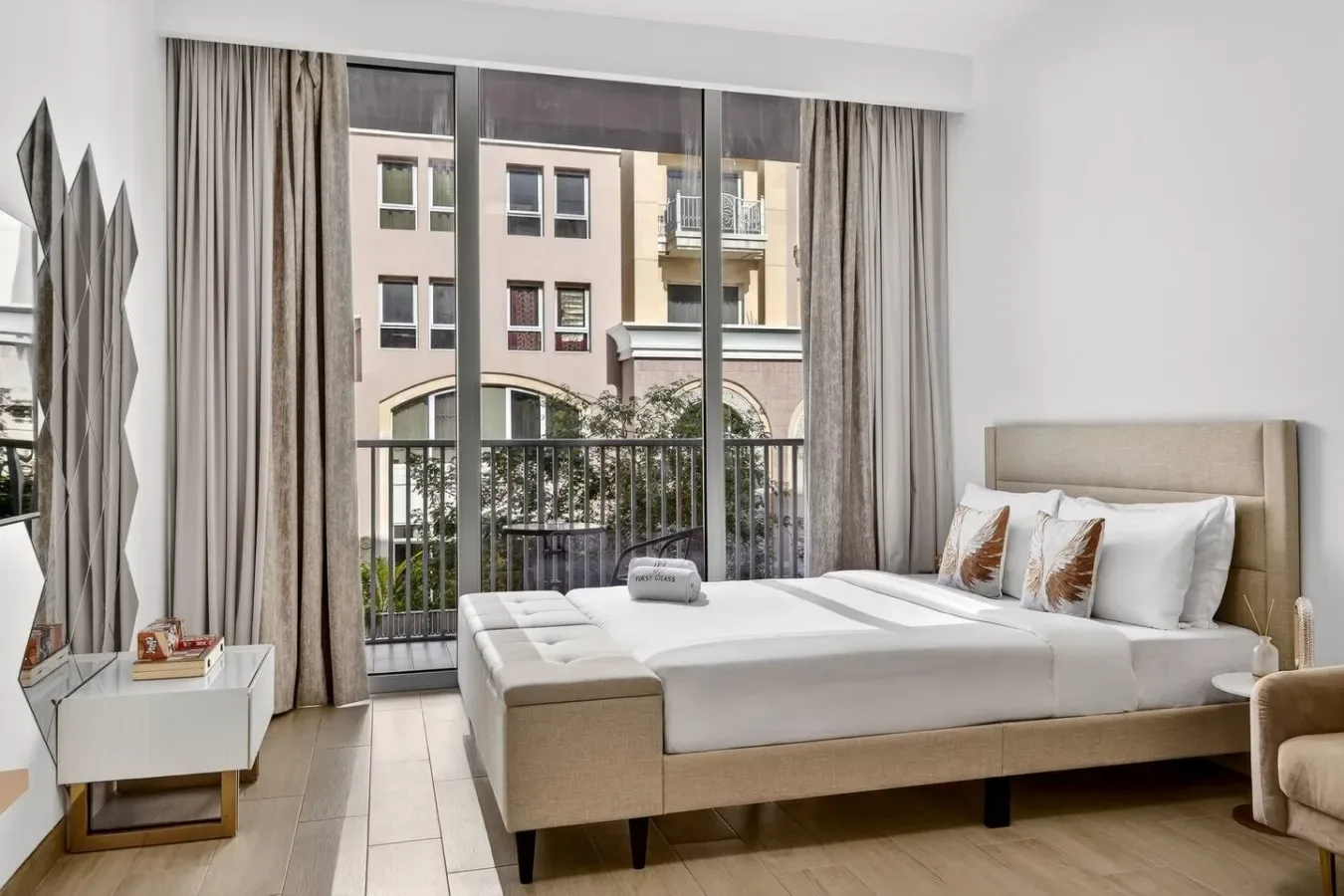 A bright bedroom with a bed beside a large window and balcony railing.