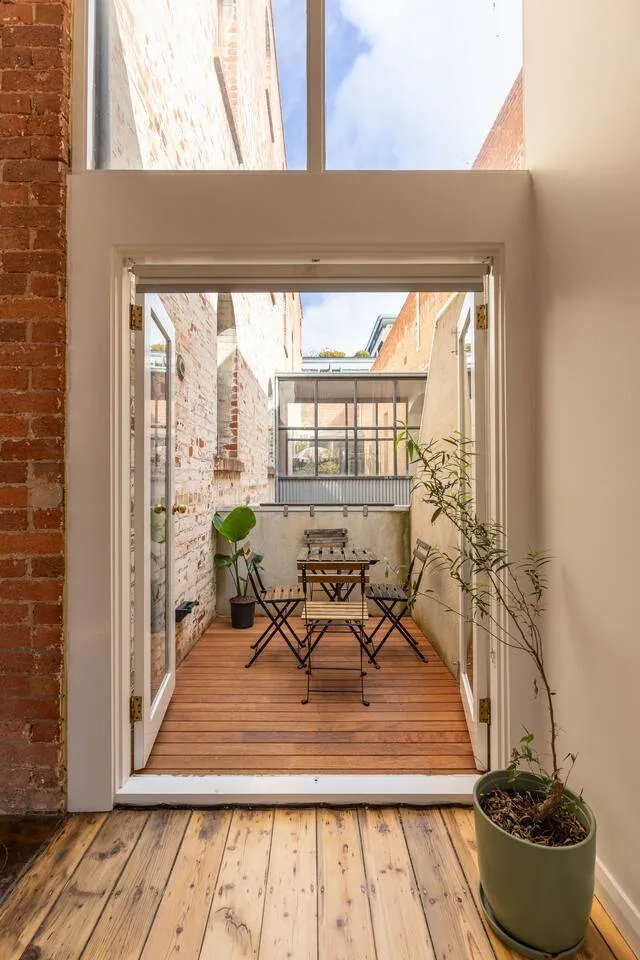 Un pequeño patio con terraza de madera, asientos al aire libre y plantas en macetas.