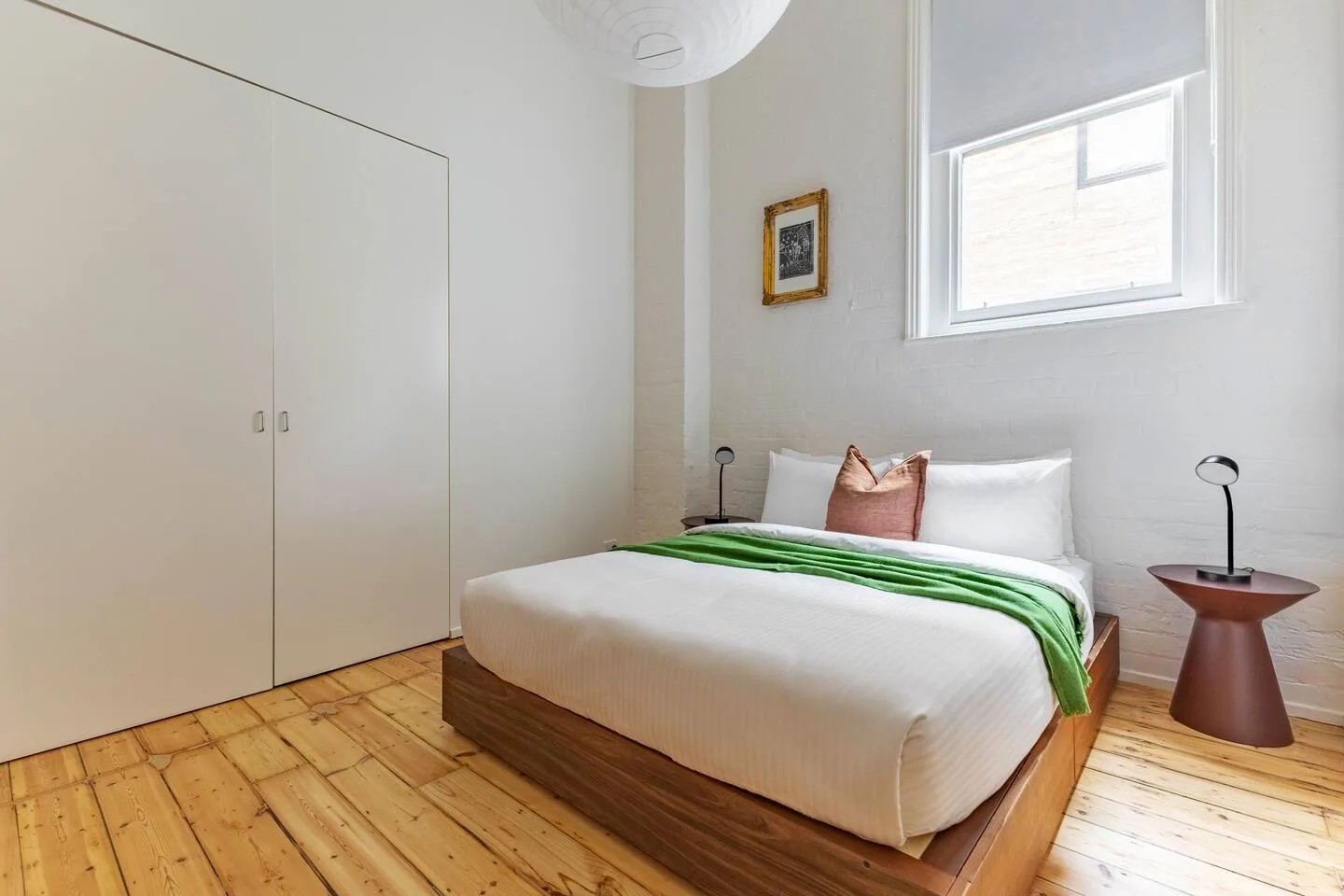 Un dormitorio con una cama vestida de blanco y verde junto a una ventana.