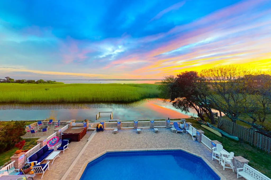 Una piscina exterior y un patio dan a una marisma bajo un cielo colorido al atardecer.