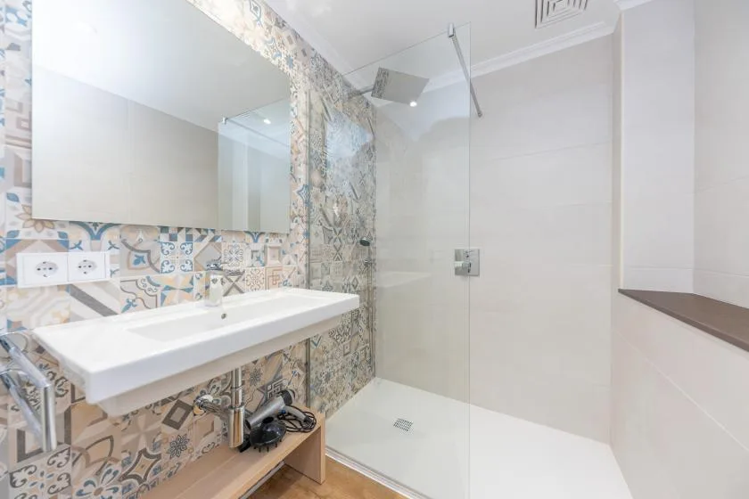A bright bathroom with a sink, patterned tile, and a glass shower.