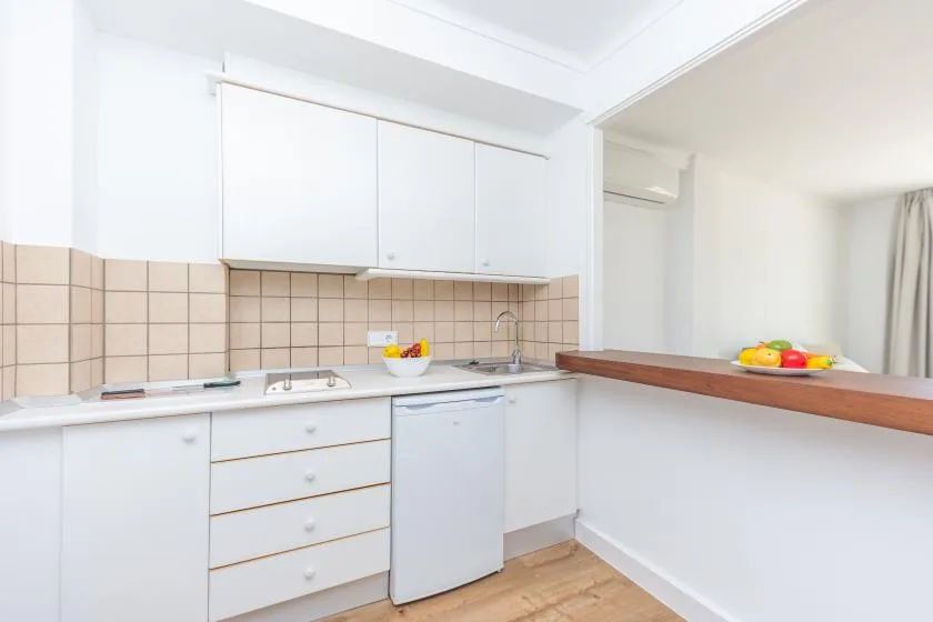 A bright kitchen with white cabinets, a tiled backsplash, and a wooden counter.