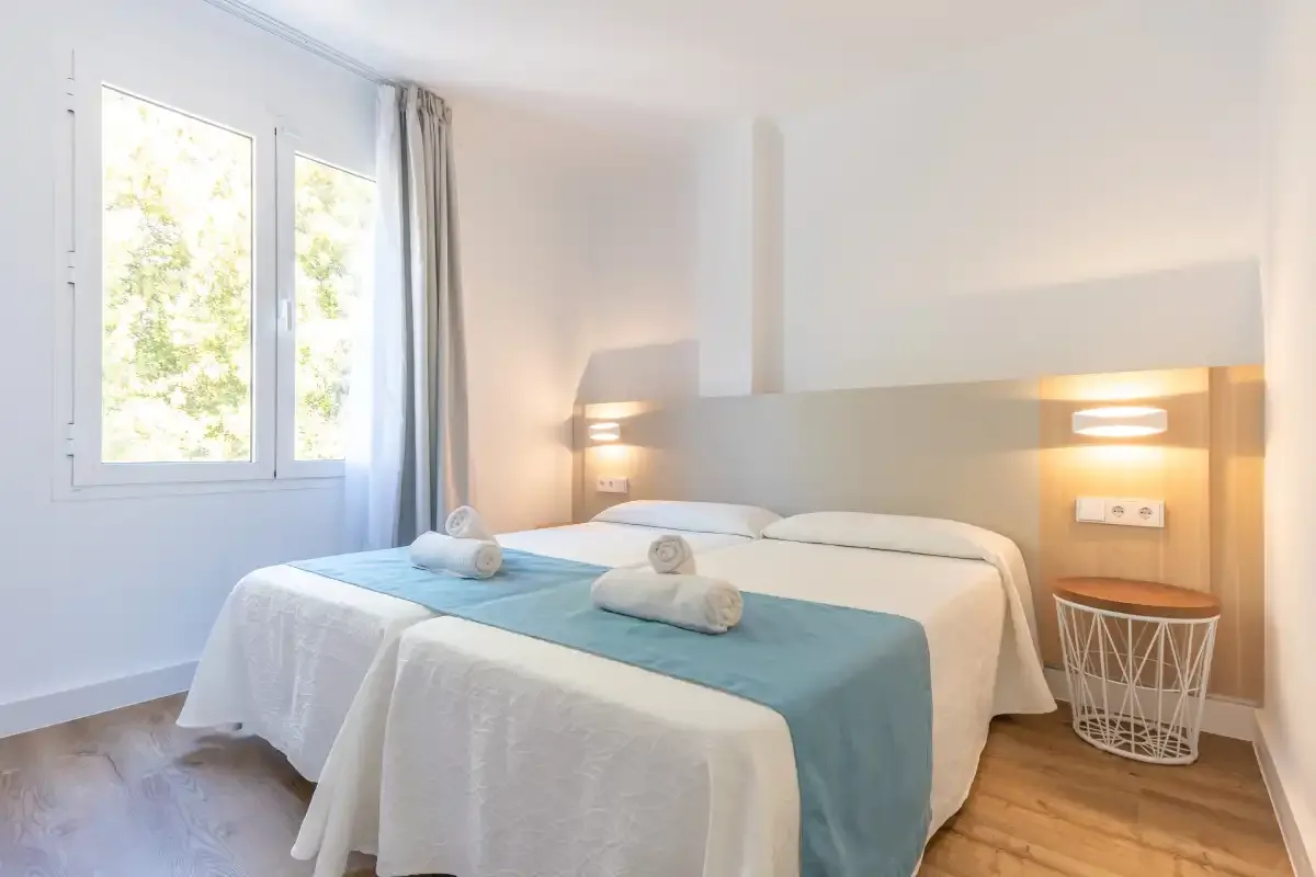 A bright bedroom with two beds, pale blue runners, and a window.