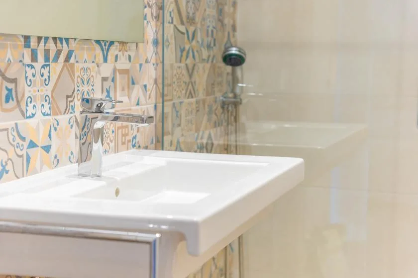 A bathroom sink and shower are set against patterned tile.