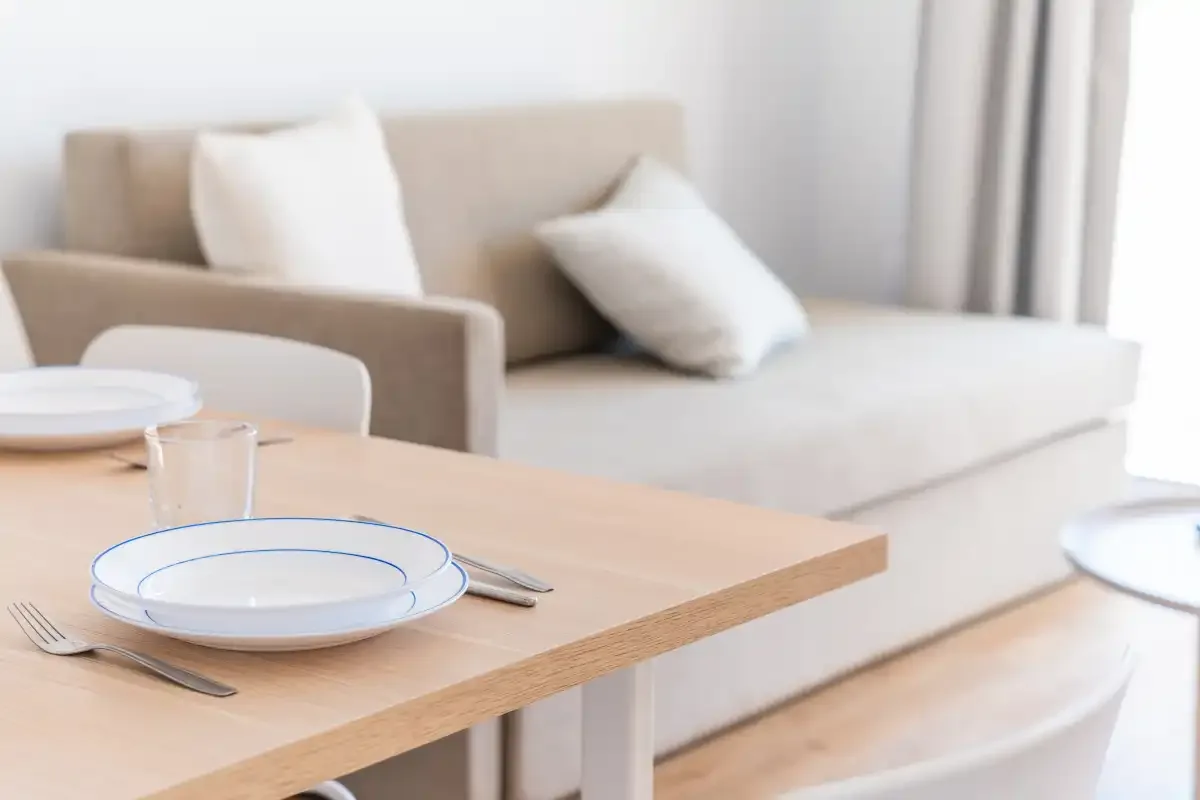 A dining table with plates and glasses sits beside a seating area.