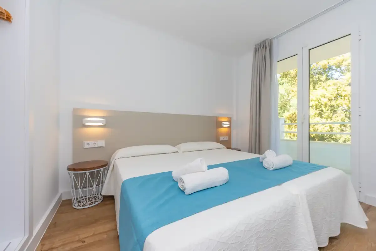 A bright bedroom with a double bed and glass doors opening onto a balcony.