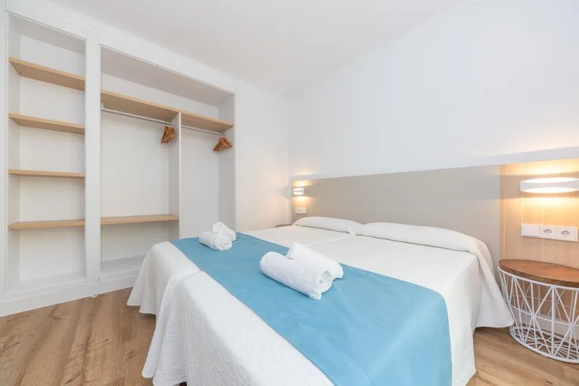 A bright bedroom with two beds and open wall shelving.
