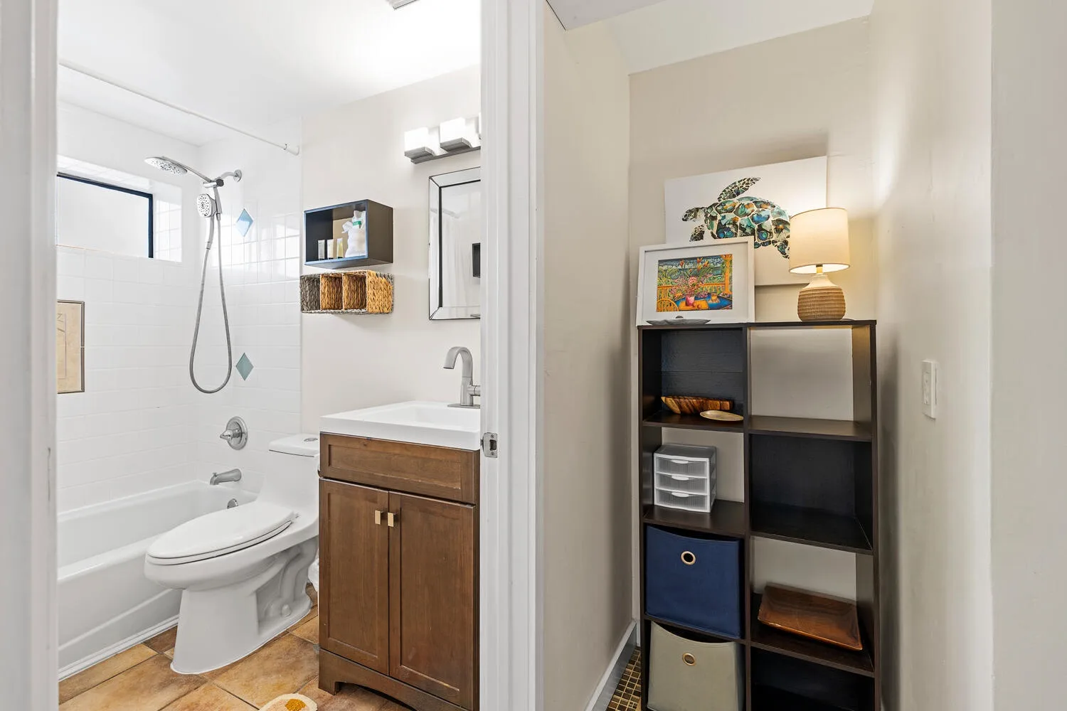 Un baño con bañera, inodoro y tocador de madera aparece junto a una estantería.
