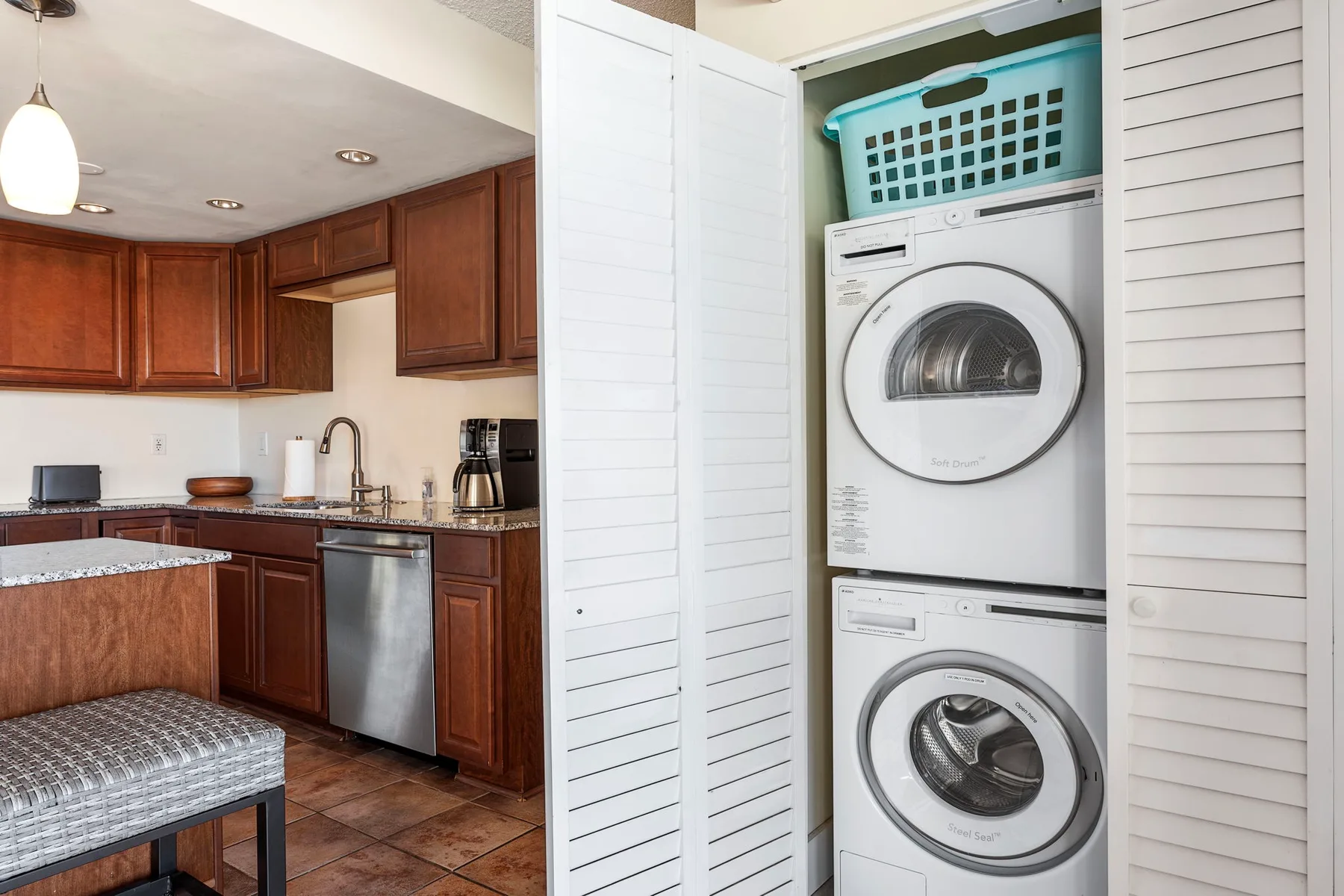 Una cocina con gabinetes de madera oscura está junto a un armario con lavadoras apiladas.